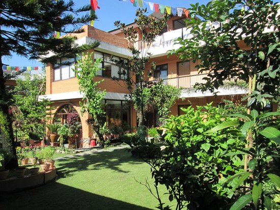 The guest house from the courtyard garden: balconies hung with prayer flags above potted plants and a green lawn