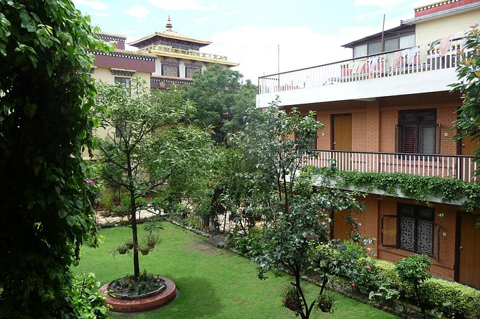 The guest house room wing seen across the lawn: two storeys of brick with wooden doors and balconies, the gilded monastery roof rising behind