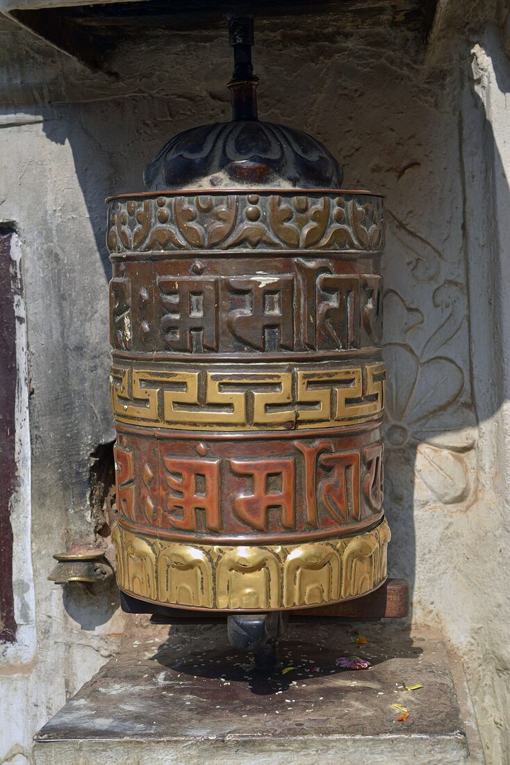 A large prayer wheel of embossed brass and copper, painted with mantras, standing in a whitewashed alcove