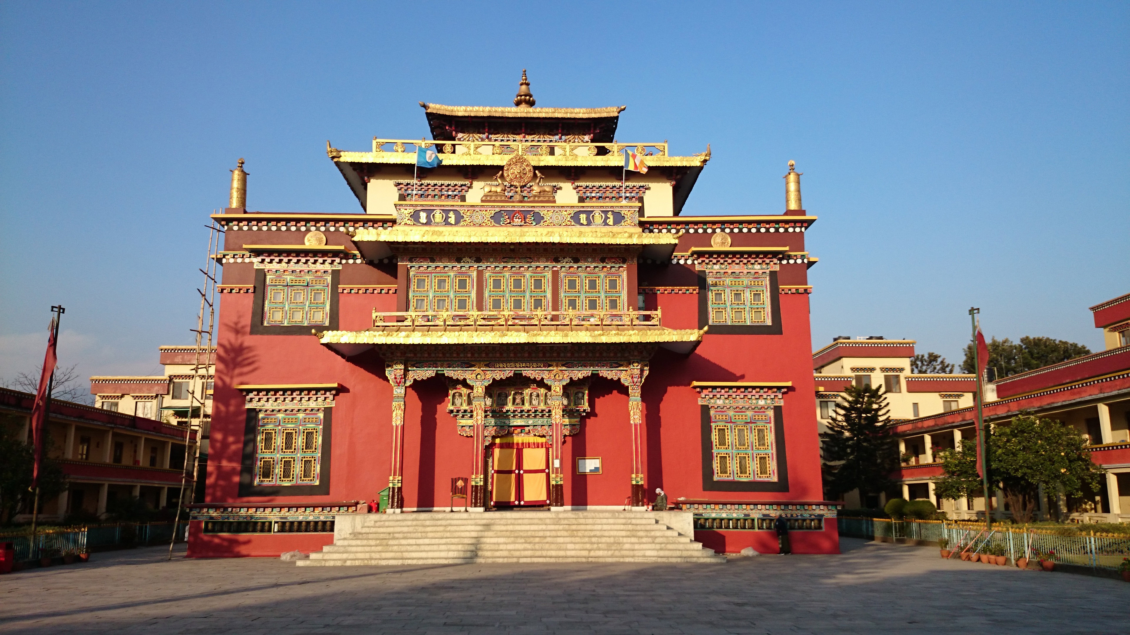 The temple of Shechen Tennyi Dargyeling in evening light: a deep red facade under gilded roofs, rows of carved and painted Tibetan windows